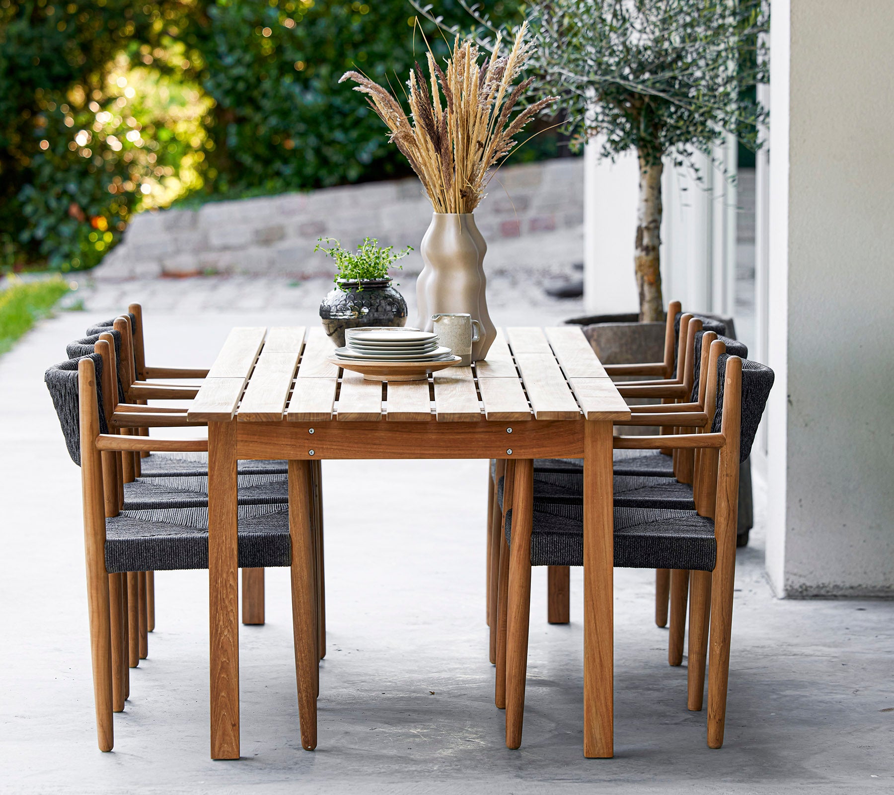 Une table en bois entourée de huit chaises élégantes, ornée d'un vase et de verdure, créant un espace de repas accueillant.
