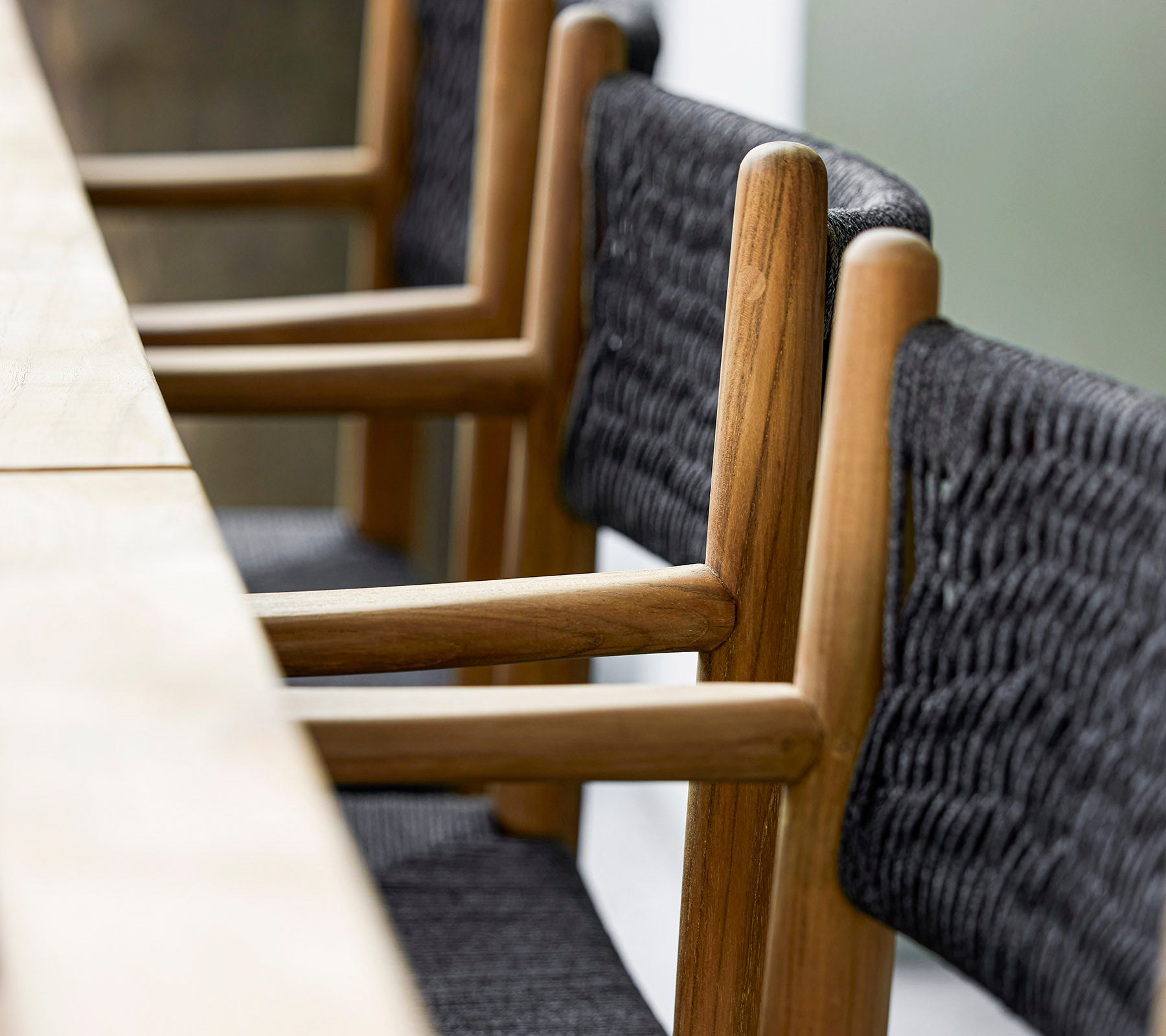 Un gros plan de chaises en bois modernes avec des détails en textile noir tressé, disposées soigneusement à côté d'une longue table en bois.