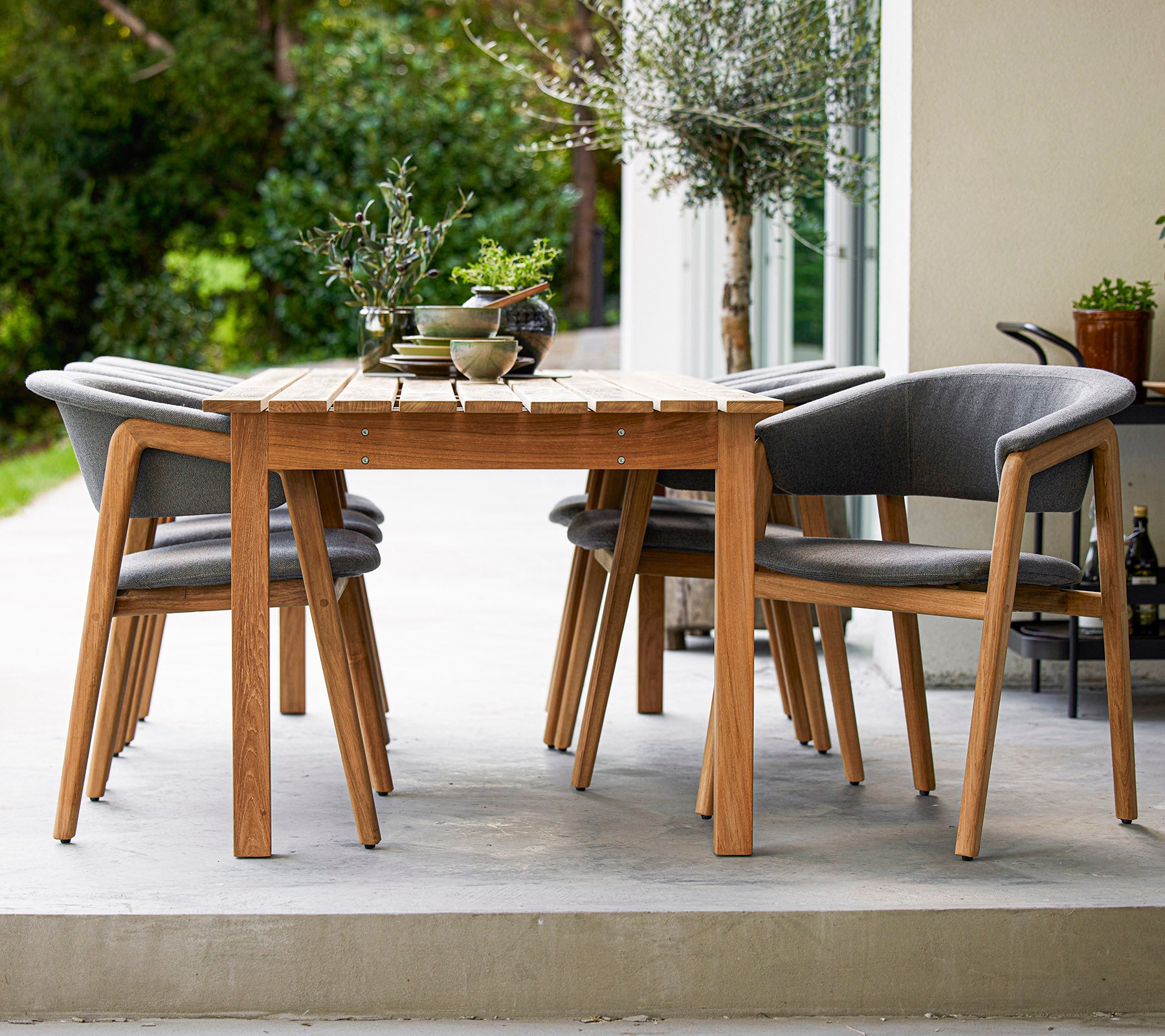 Une table à manger en bois au style élégant entourée de quatre chaises grises rembourrées, parfaite pour des rassemblements en plein air.