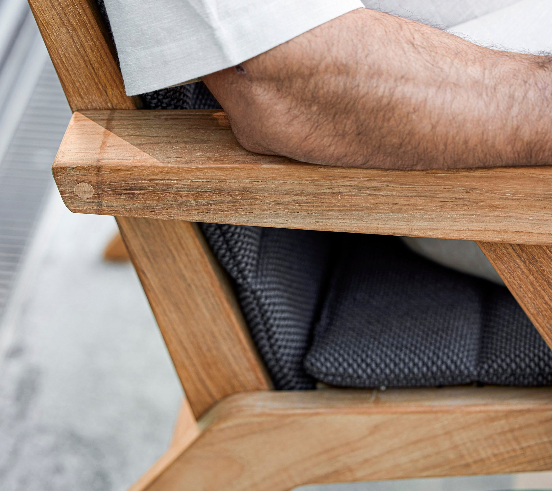 Un gros plan d'un accoudoir de chaise en bois avec un siège rembourré, présentant un bras reposant dessus, mettant en valeur un mélange de matériaux naturels et texturés.