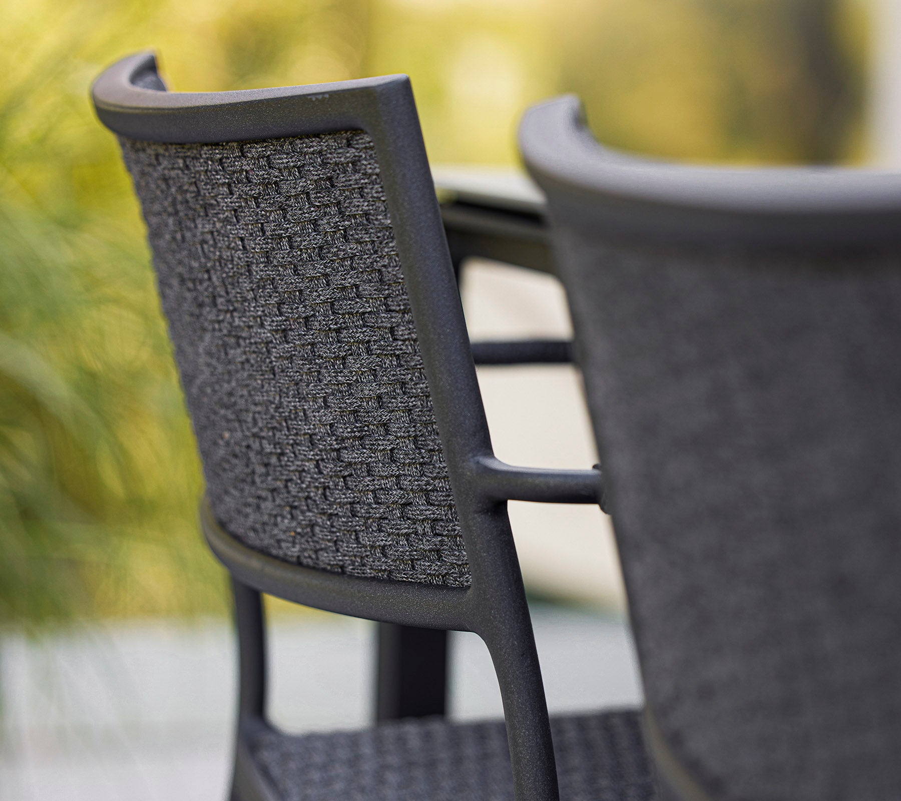 Gros plan sur une chaise élégante avec un dossier tissé, présentant un design moderne dans des teintes de gris. Parfaite pour des espaces contemporains.