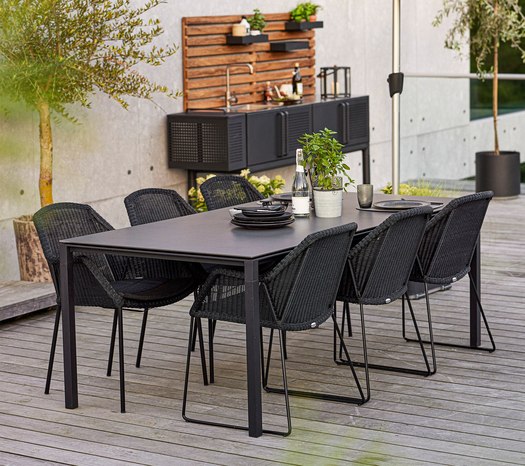 Un ensemble de salle à manger moderne comprenant une table rectangulaire et six chaises élégantes, complété par des plantes décoratives et de la vaisselle.