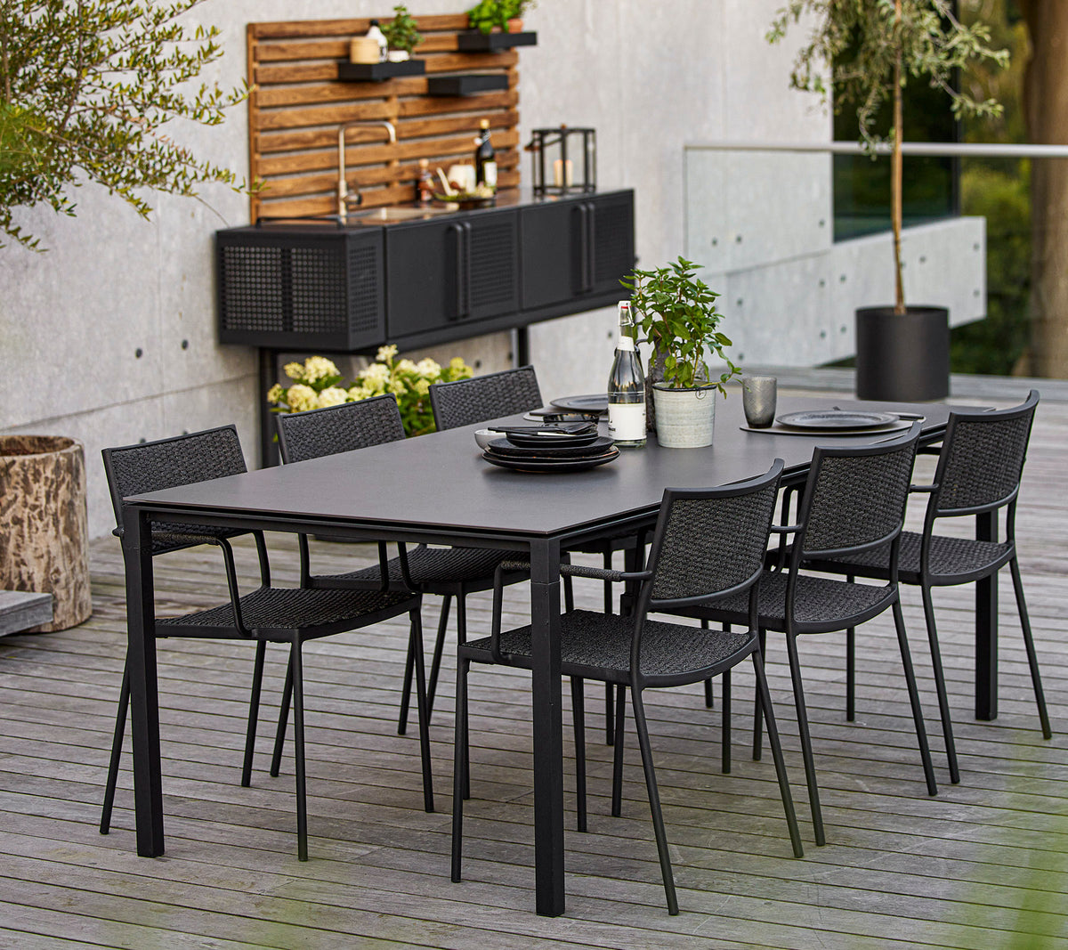 Un ensemble de salle à manger moderne comprenant une grande table rectangulaire et six chaises en osier noires, rehaussé d'éléments décoratifs et de verdure.