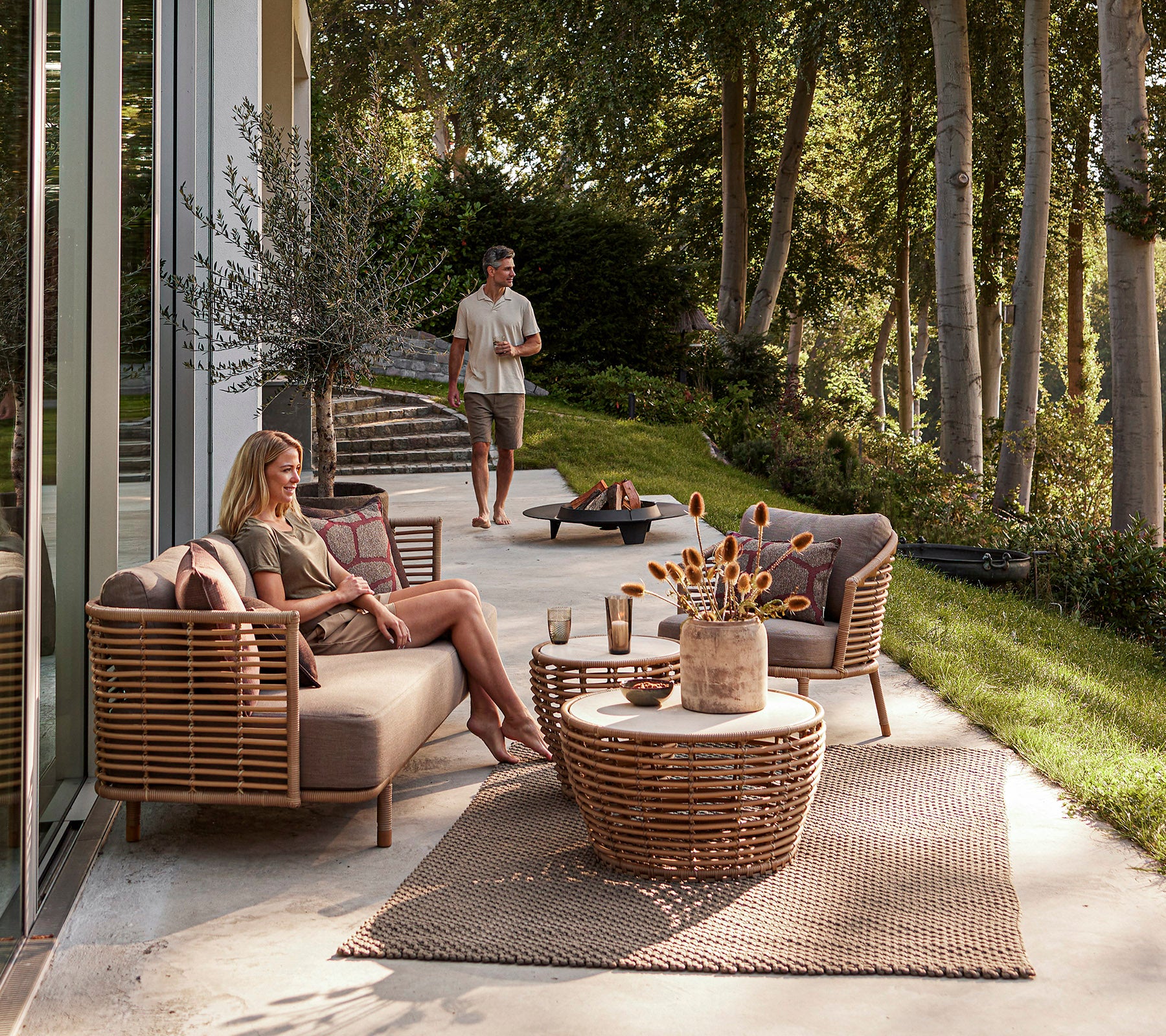 Un espace extérieur élégant avec des meubles tissés, une table basse décorative et une atmosphère détendue avec de la verdure en arrière-plan.
