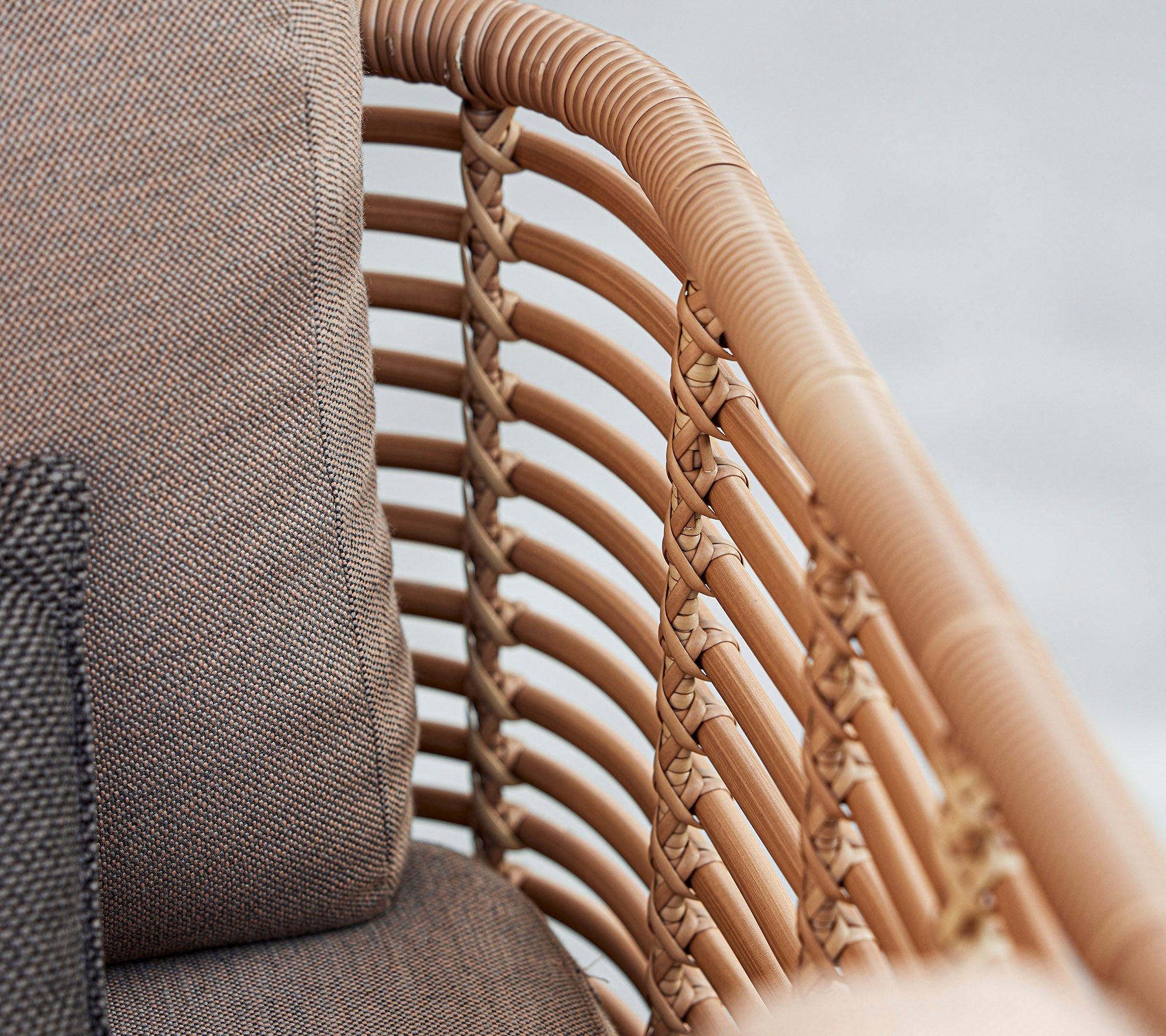 Gros plan d'un fauteuil élégant avec des détails en rotin tressé et des coussins doux dans des tons neutres, mettant en valeur un design moderne.