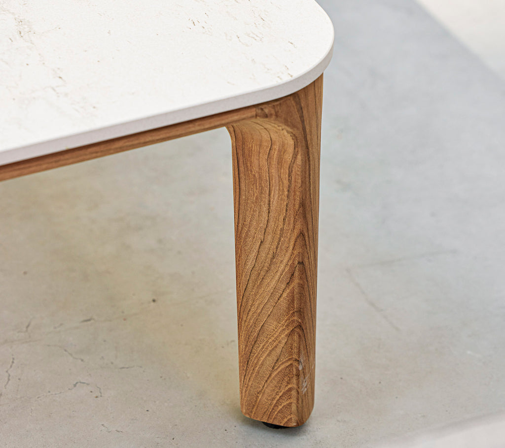 Un gros plan d'une table avec une jambe en bois texturée et un plateau lisse et blanc. Des éléments de design élégants et modernes sont mis en avant.