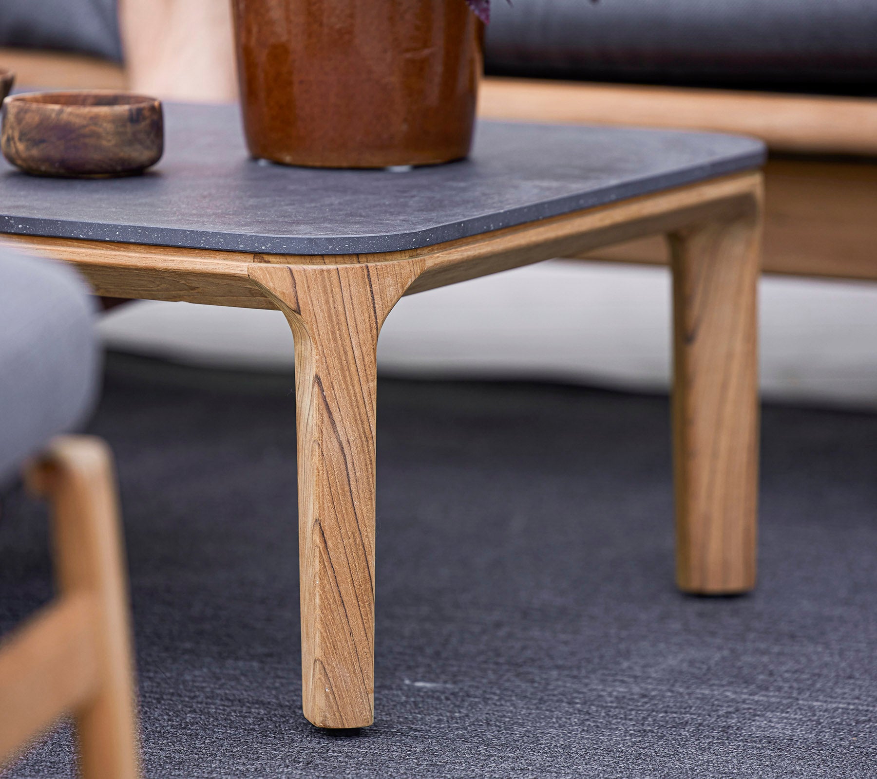 Une table en bois avec un plateau en pierre sombre, dotée de pieds sculptés de manière unique, entourée de sièges moelleux et d'un pot de plante décoratif.