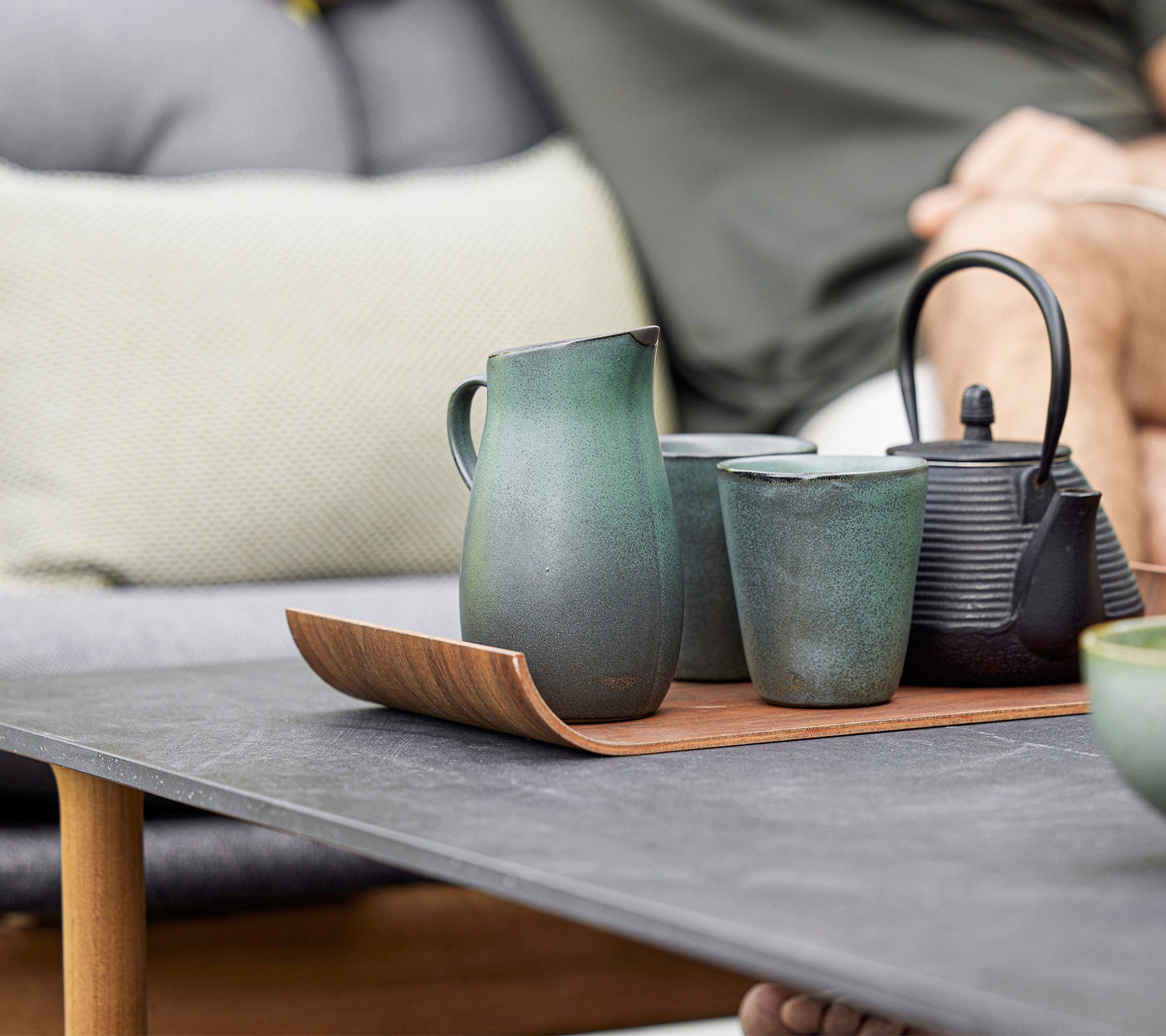 Une arrangement élégant de théière en céramique, tasses et une carafe sur un plateau en bois, mettant en valeur le design moderne et les tonalités terreuses.
