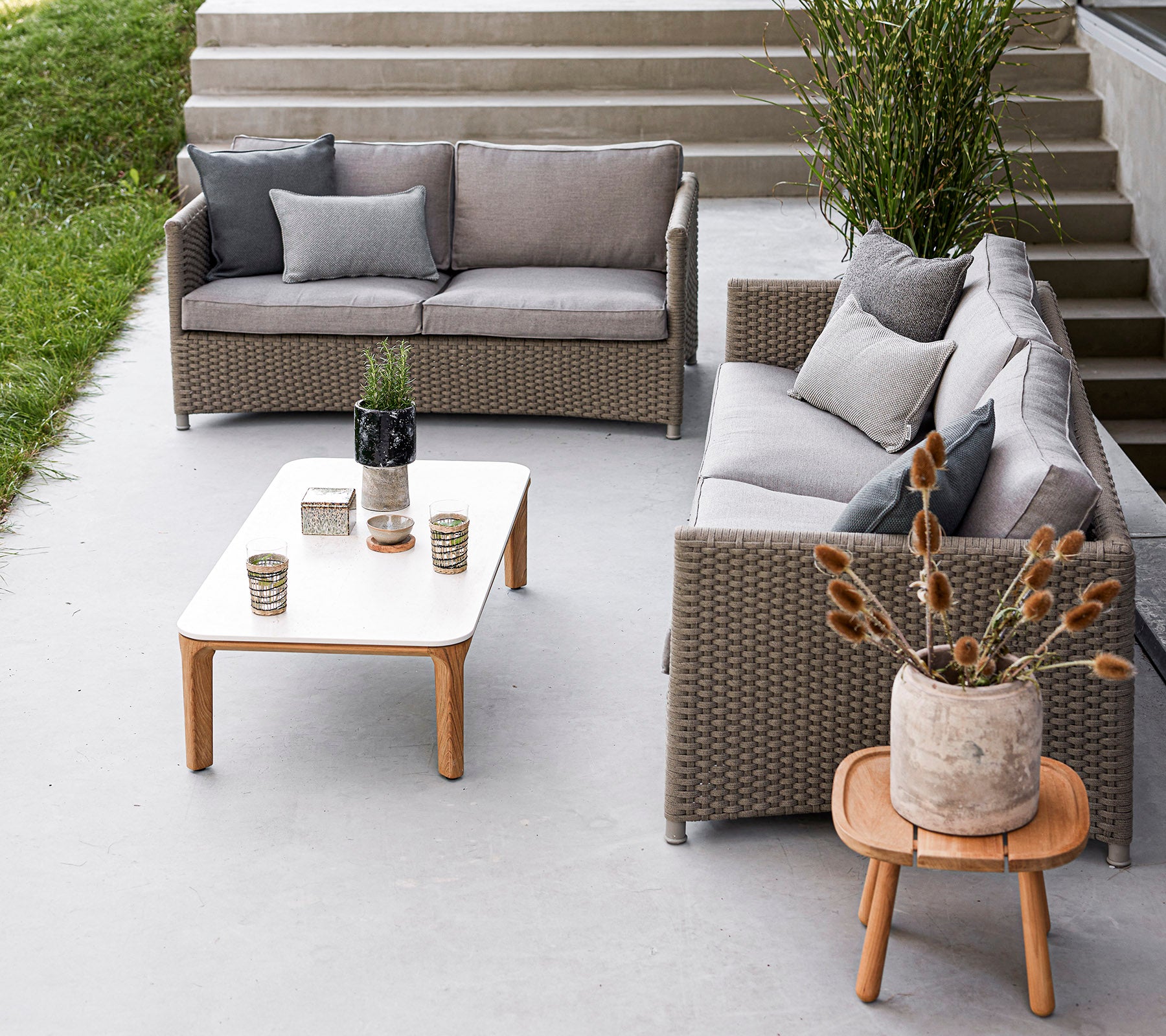 Agencement de sièges extérieur élégant avec un ensemble de canapés gris, une table en bois, des vases décoratifs et des plantes en pot. Idéal pour se détendre.