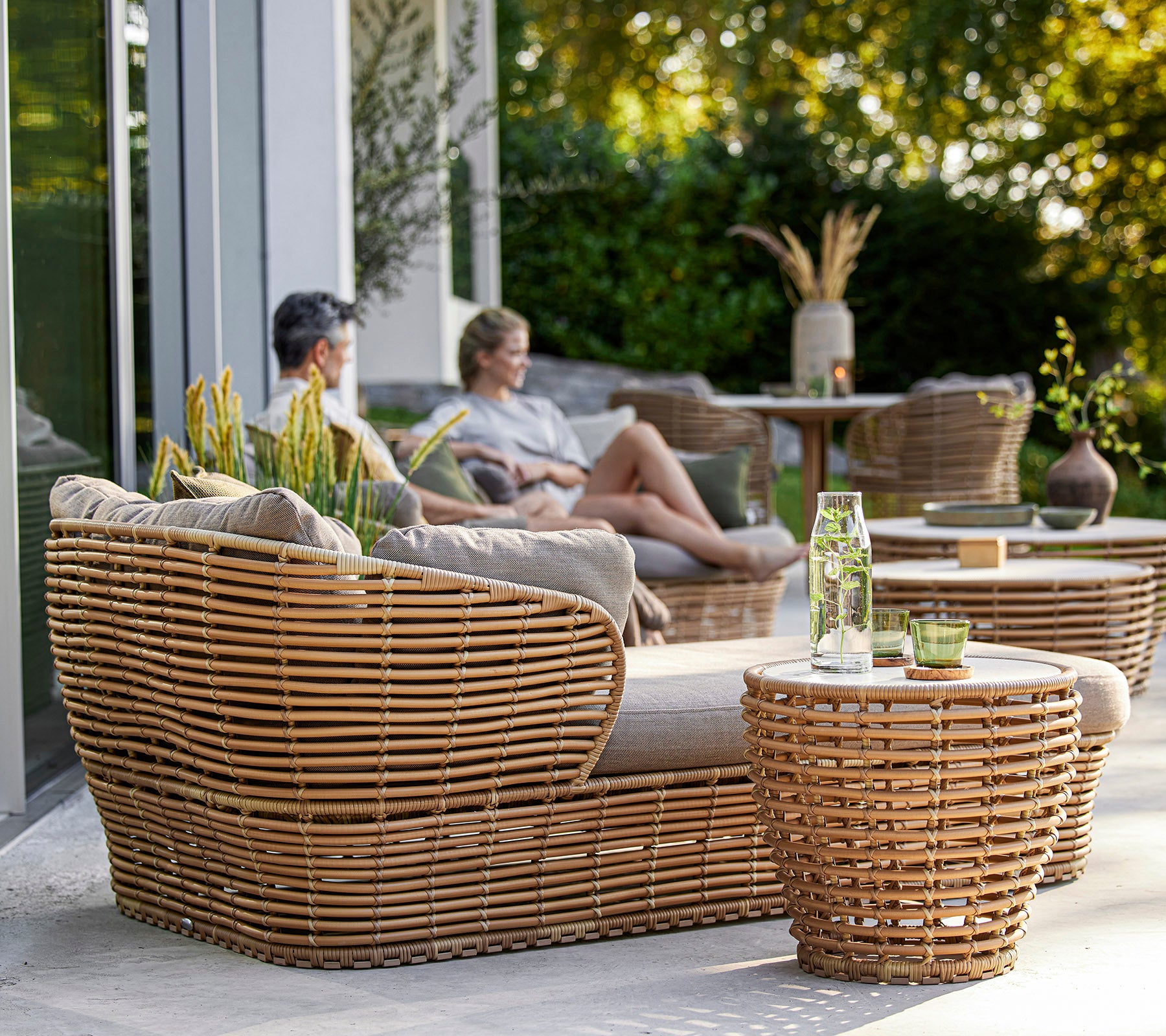 Ensemble de meubles tissés élégant comprenant un coin salon confortable et des tables, complété par des plantes décoratives et une atmosphère détendue.