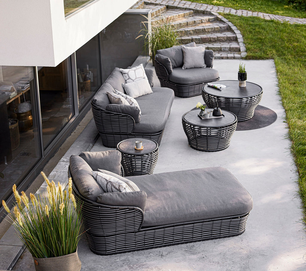Aménagement extérieur élégant avec un canapé sectionnel gris, des fauteuils et des tables, complété par des coussins décoratifs et des plantes.