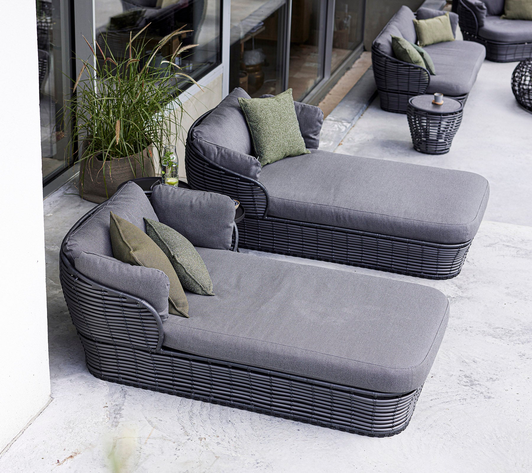 Deux fauteuils modernes avec des coussins gris pelucheux et des coussins d'appoint verts, accompagnés d'une table d'appoint ronde.