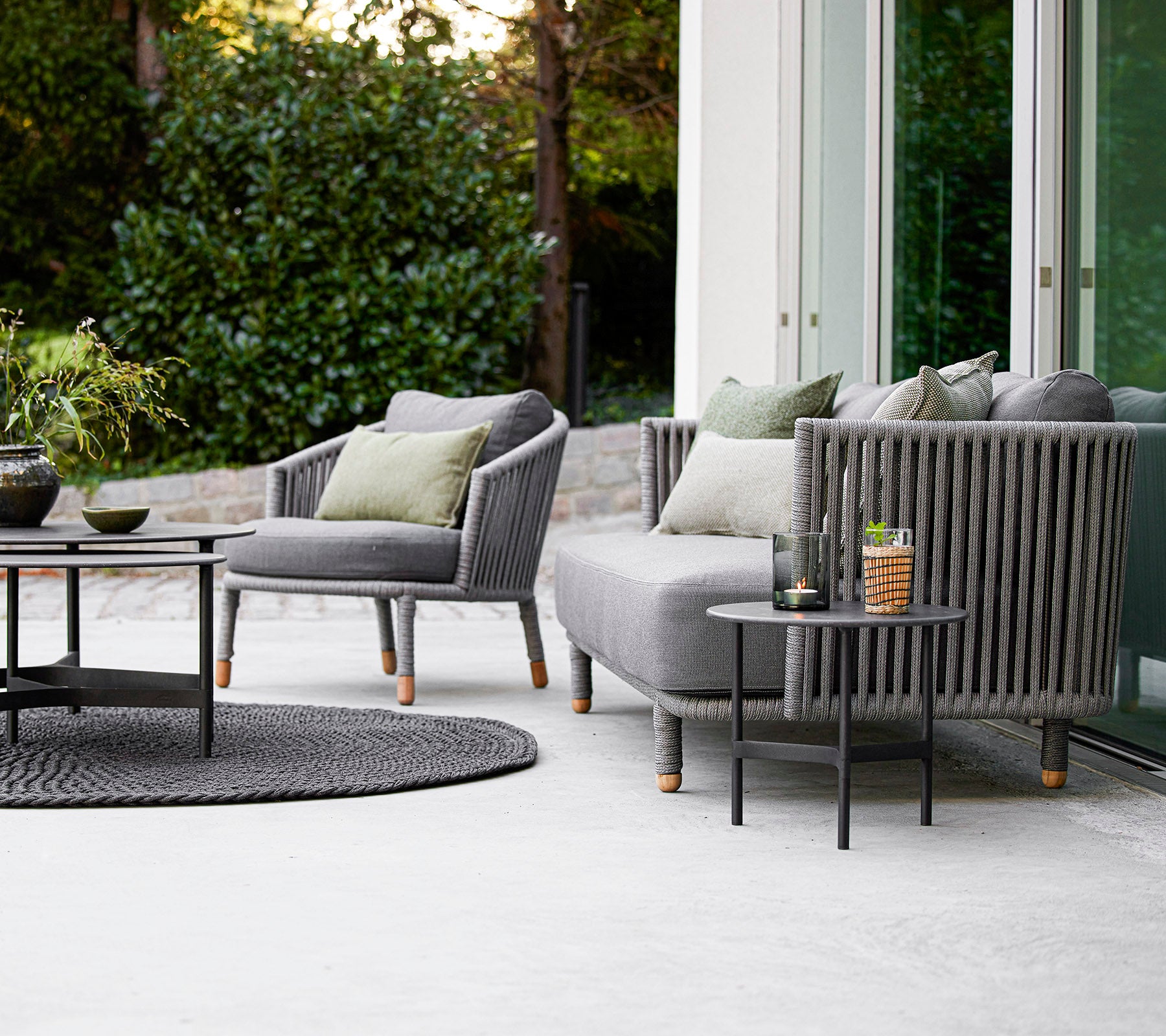 Ensemble d'extérieur contemporain comprenant un canapé et des fauteuils avec des coussins, accompagné d'une table basse ronde et d'accessoires décoratifs.