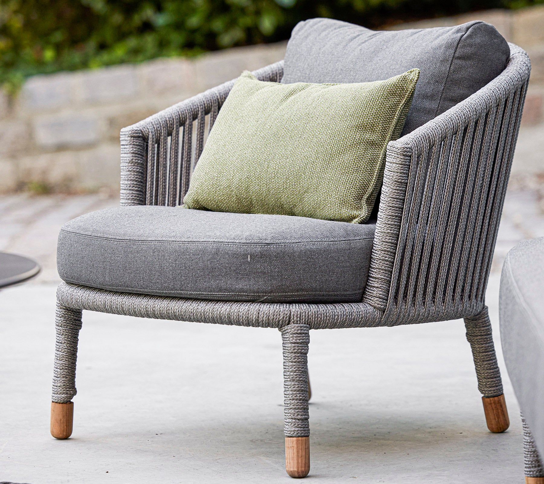 Fauteuil grise élégante avec un design arrondi et un coussin vert confortable, en tissu texturé et pieds en bois naturel. Parfait pour se détendre.