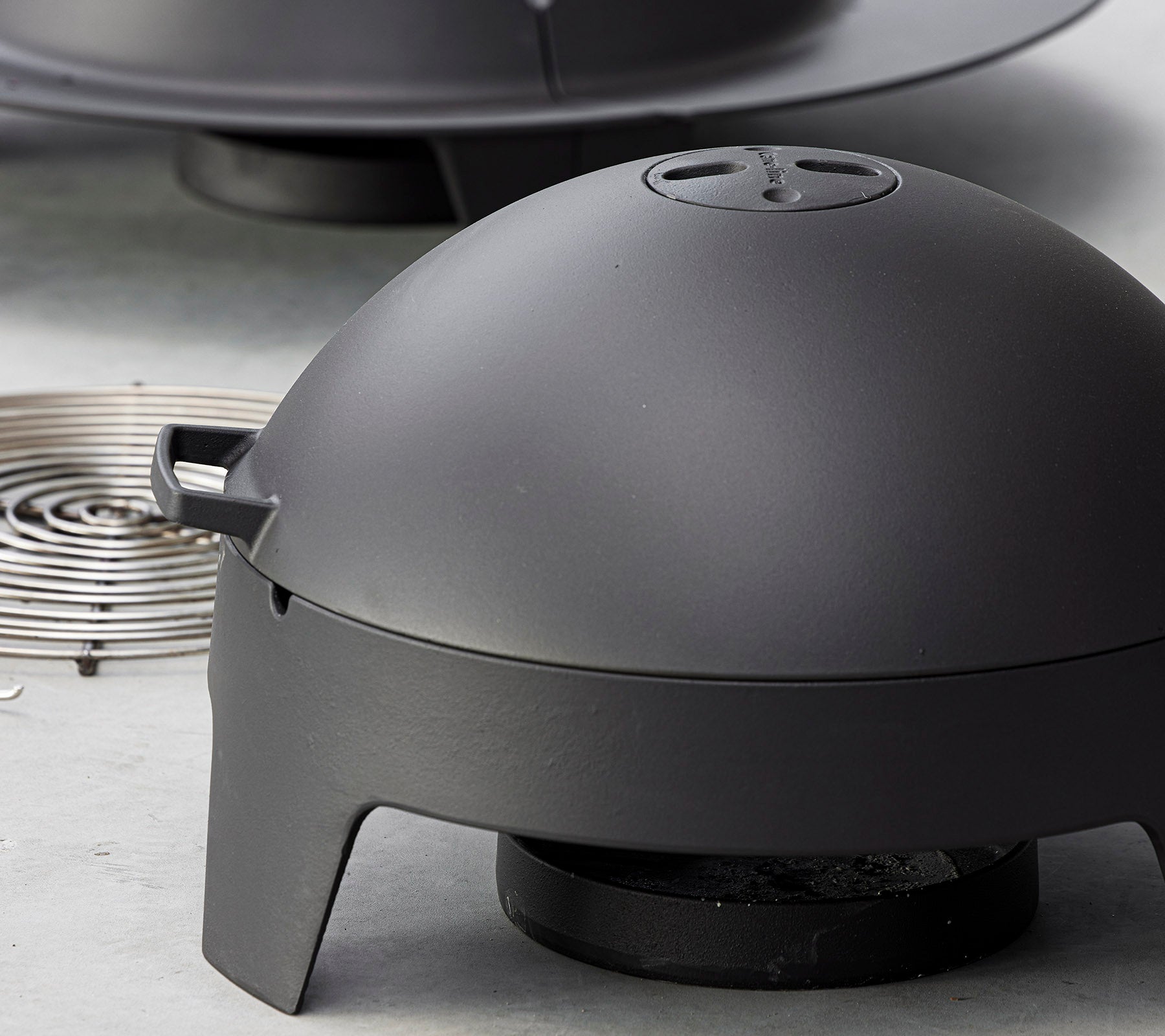 Appareil de cuisson noir mat avec un couvercle en forme de dôme et une source de chaleur amovible, conçu pour le grillage et le barbecue en extérieur.