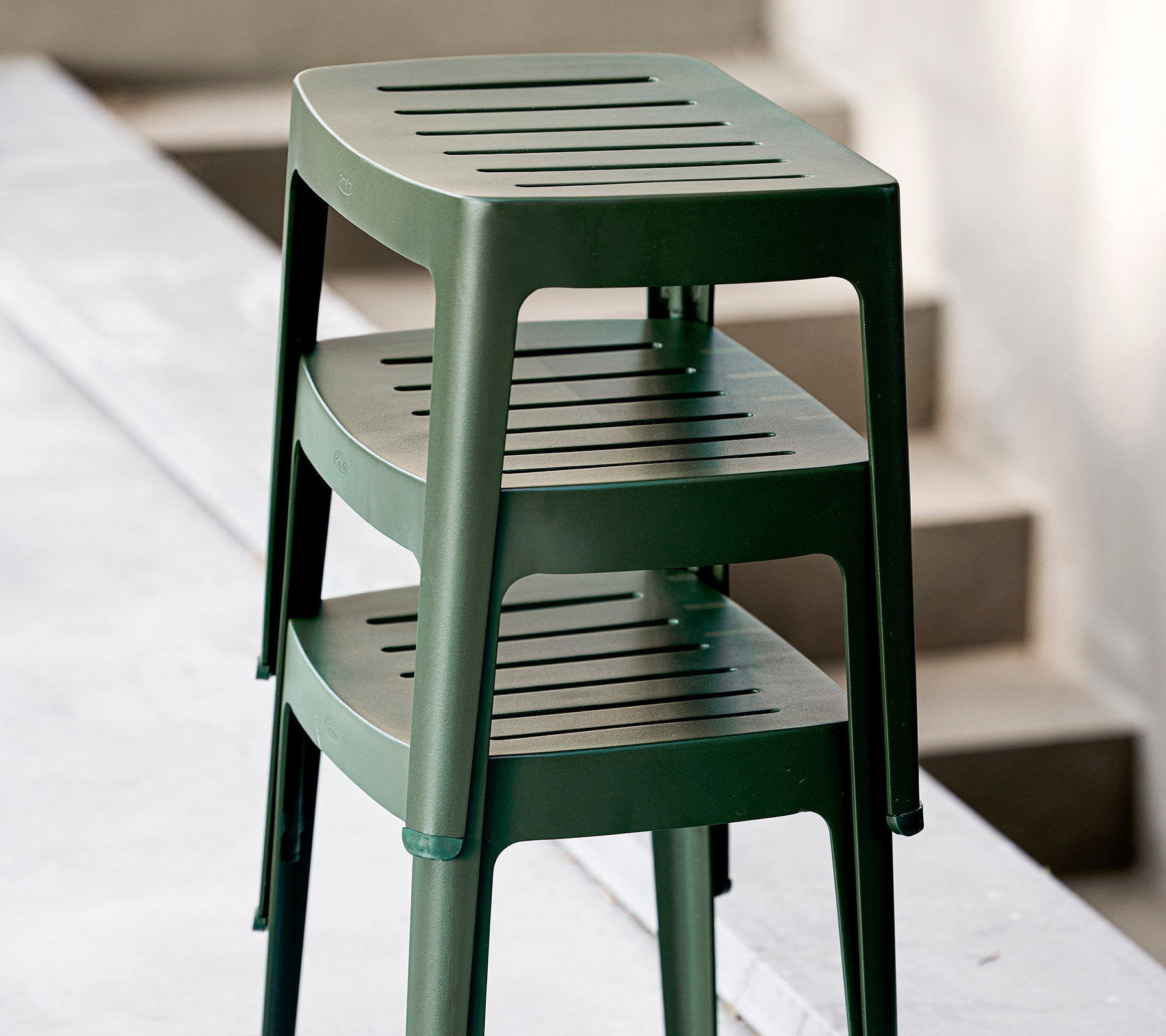 Tabourets en plastique vert empilables avec sièges fendus, conçus pour un usage décontracté. Idéaux pour des agencements de sièges polyvalents.