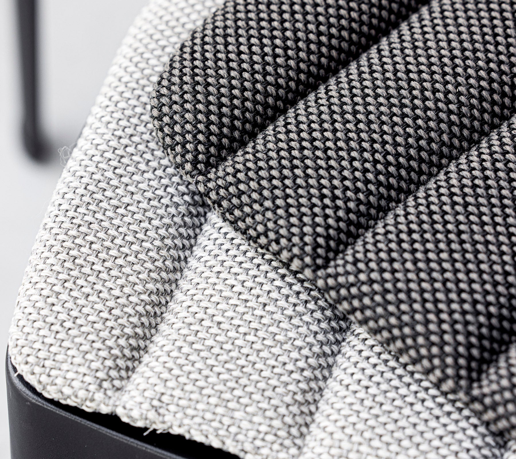 Gros plan d'un siège en tissu texturé, présentant un mélange de motifs tissés gris clair et gris foncé avec un design moderne. Idéal pour des intérieurs contemporains.