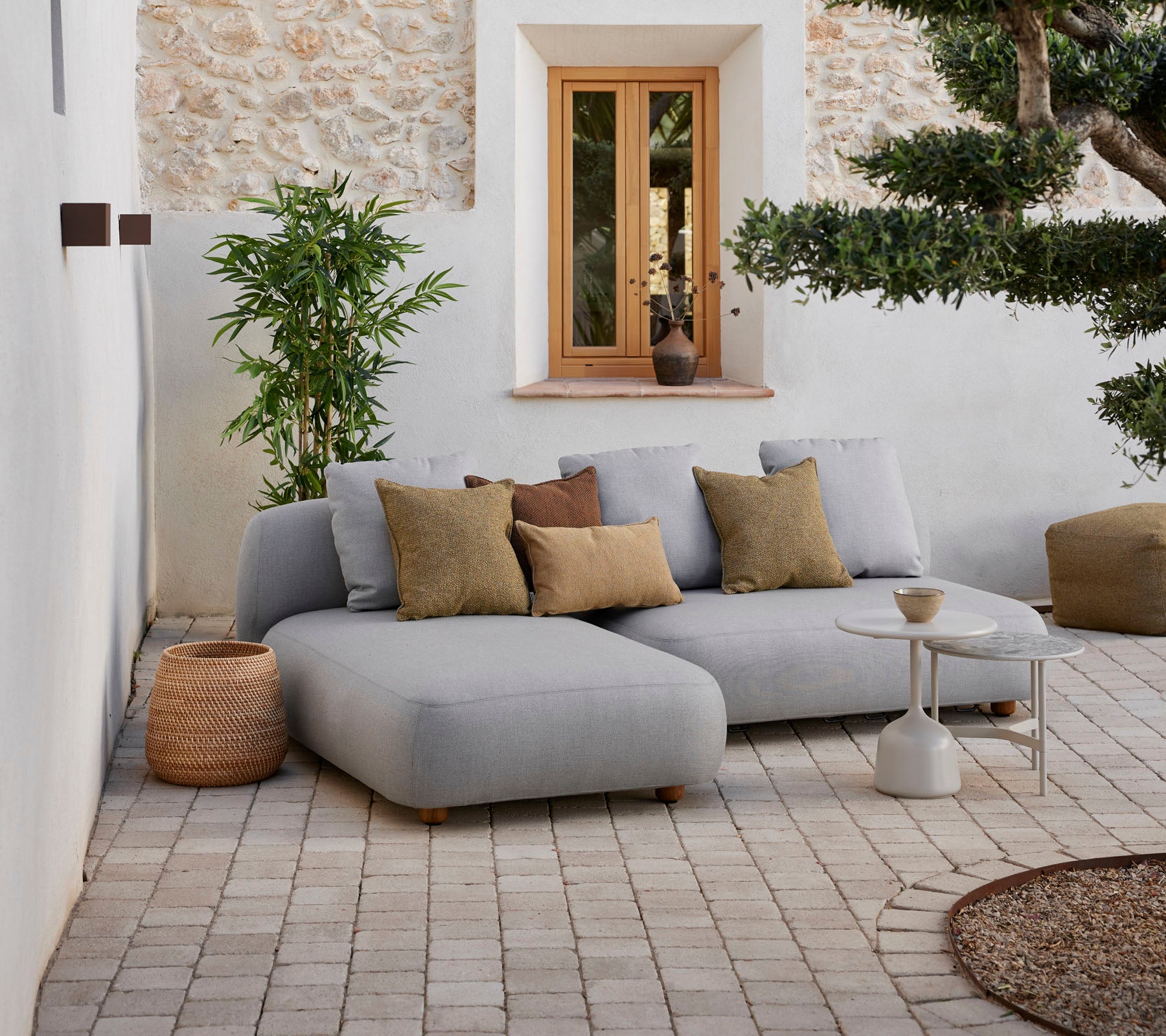 Canapé sectionnel gris moderne avec des coussins décoratifs, petite table d'appoint et éléments naturels dans un cadre chaleureux.