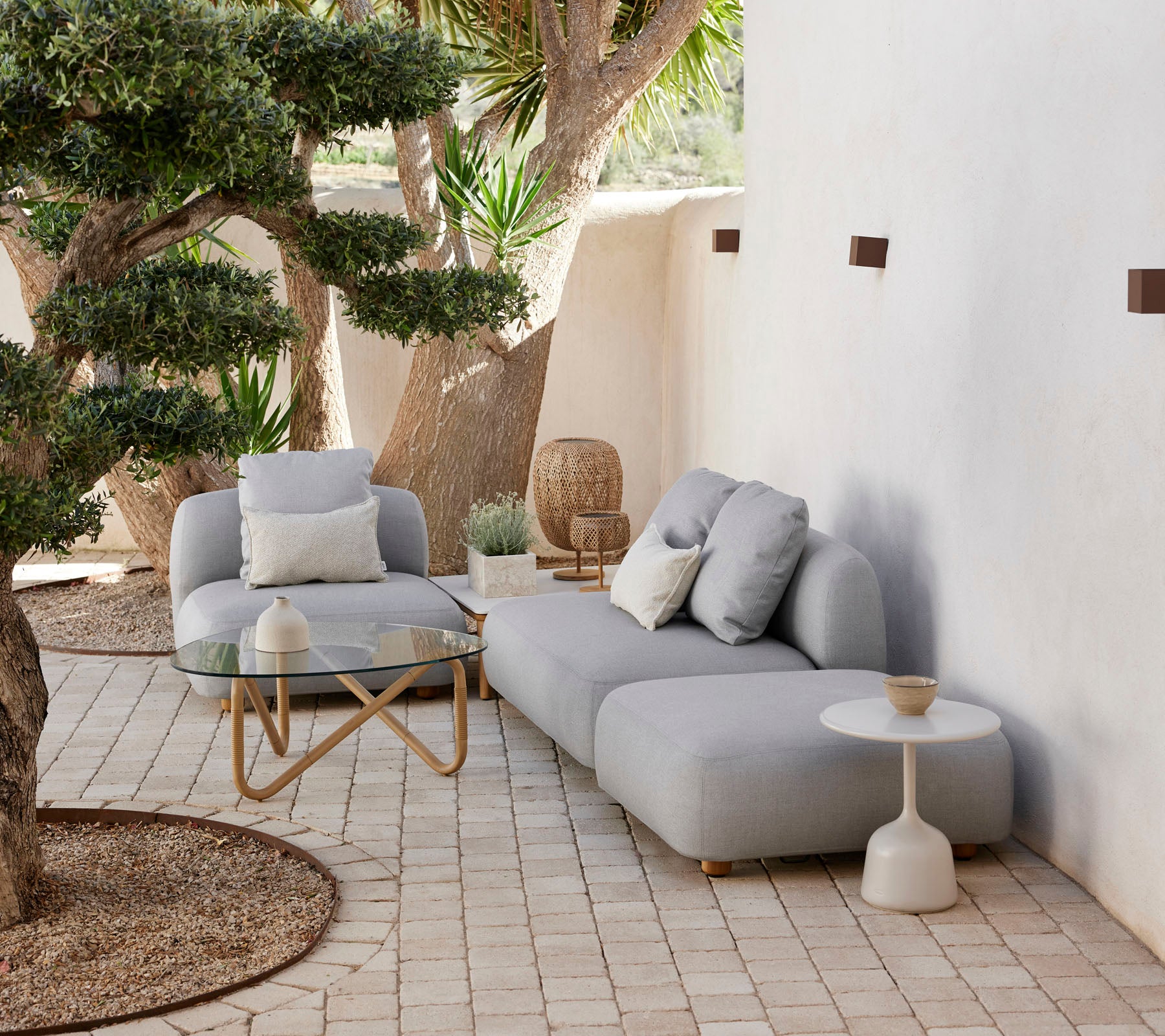 Aménagement extérieur moderne avec un canapé confortable, une chaise accent et une table d’appoint élégante, entouré de verdure et d’éléments décoratifs.