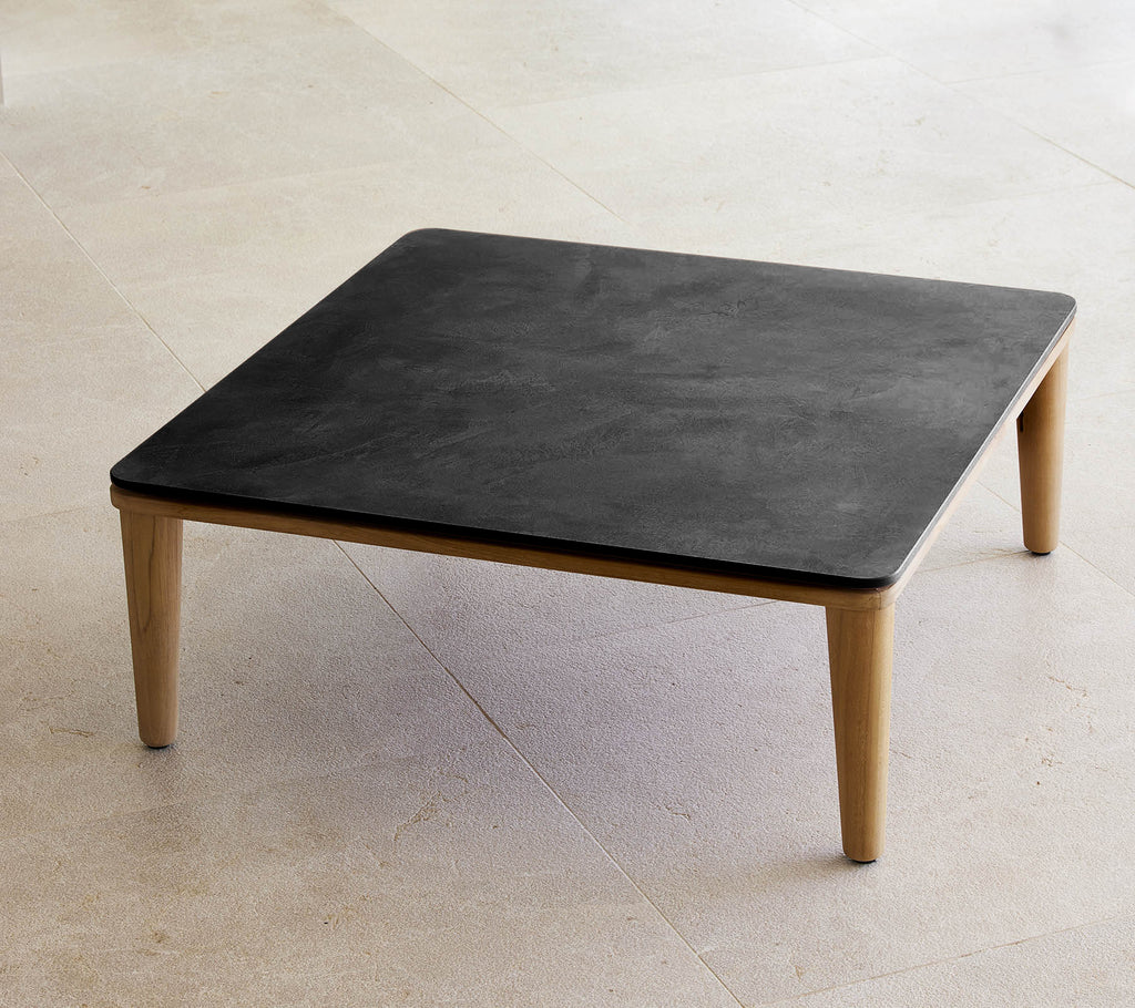 Table carrée noire avec des pieds en bois dans un cadre minimaliste.