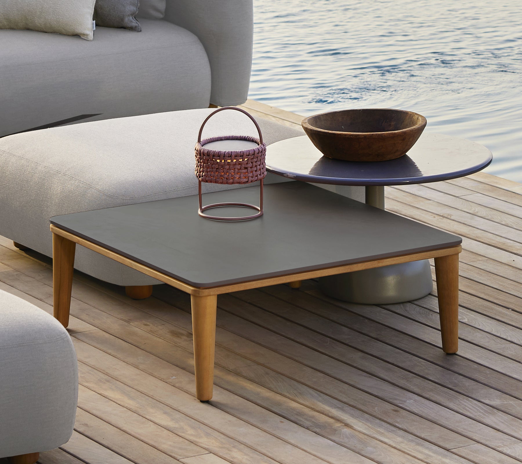 Table grise moderne avec un bol en bois et un panier en métal dans un cadre extérieur.