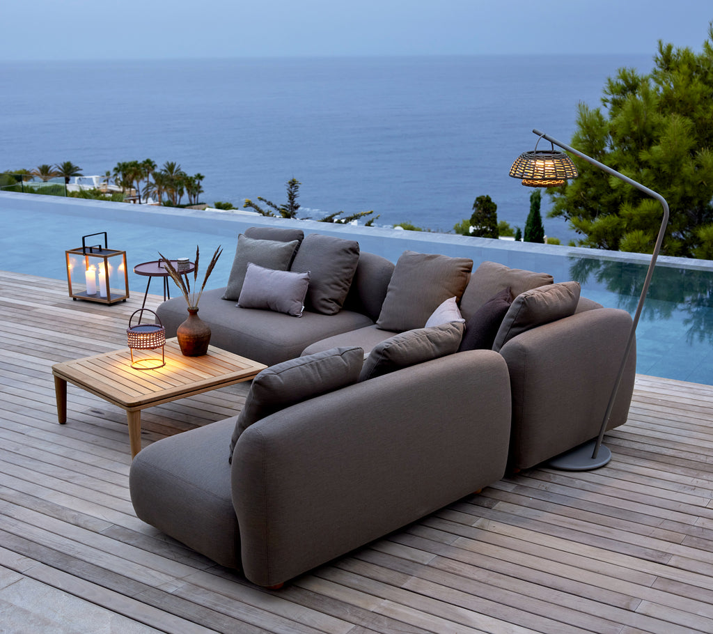Sofa gris avec table en bois et lanternes au bord de la piscine surplombant l'océan.
