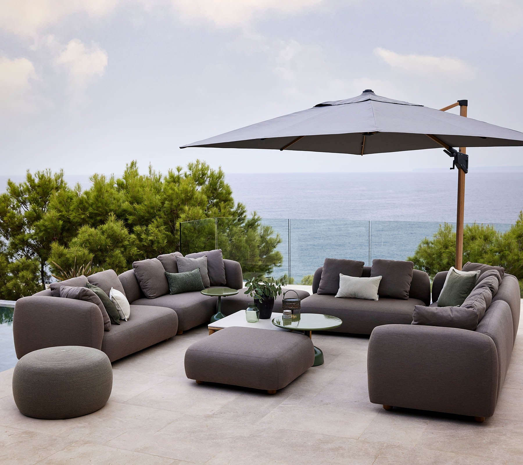 Ensemble de salon moderne avec des coussins moelleux, accompagné d'une table ronde et d'un grand parasol, entouré de verdure et d'une vue pittoresque.