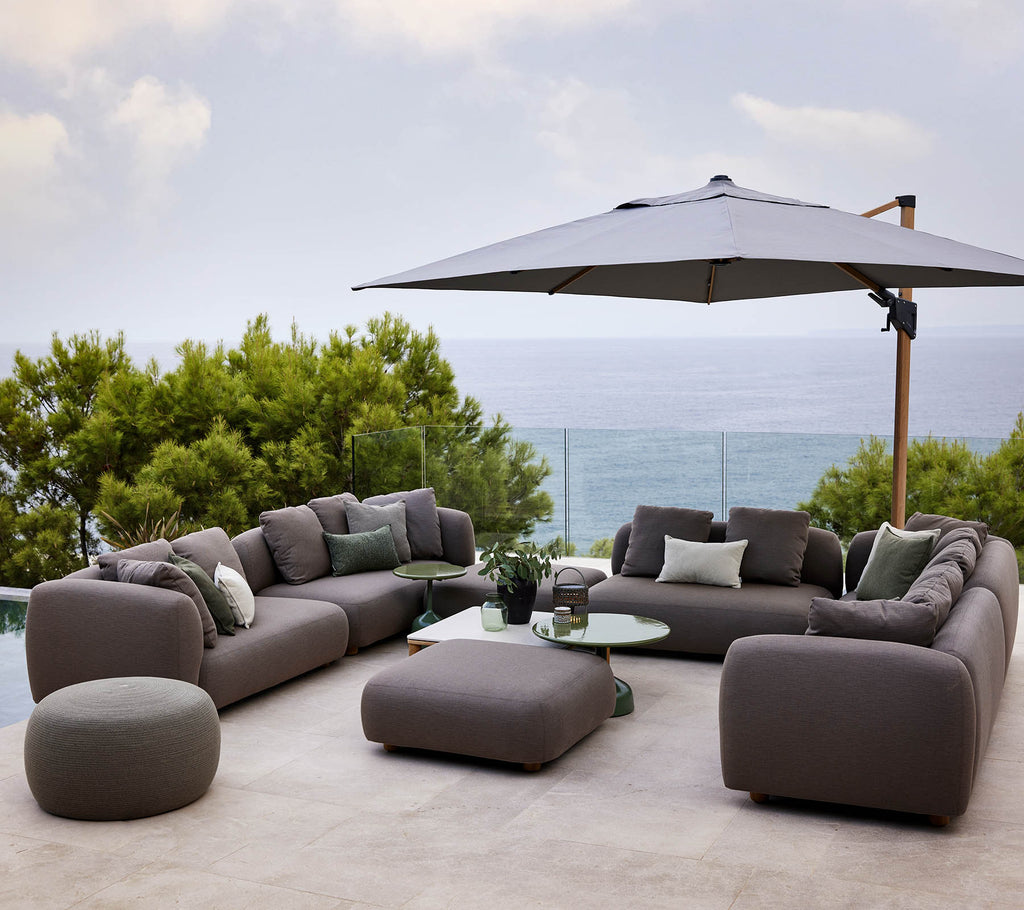 Ensemble de salon moderne avec des coussins moelleux, accompagné d'une table ronde et d'un grand parasol, entouré de verdure et d'une vue pittoresque.