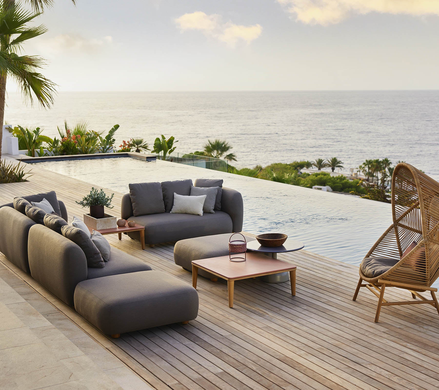 Espace lounge élégant avec une chaise suspendue en forme de ruche et des sièges modernes, complété par une vue panoramique sur l'océan et une verdure luxuriante.