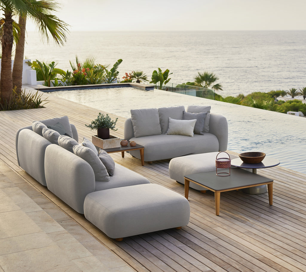 Canapé gris élégant avec des coussins et une table basse noire dans un salon extérieur moderne au bord de la mer.