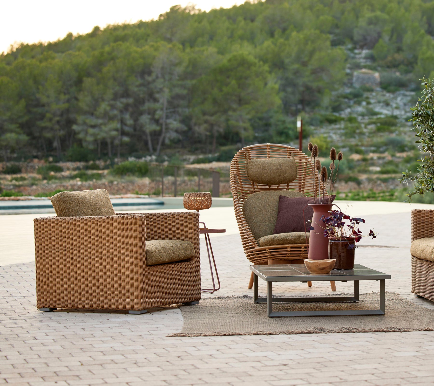 Un agencement de sièges confortable avec des chaises en osier, une table d'appoint et un vase décoratif, entouré de verdure et de paysages naturels.