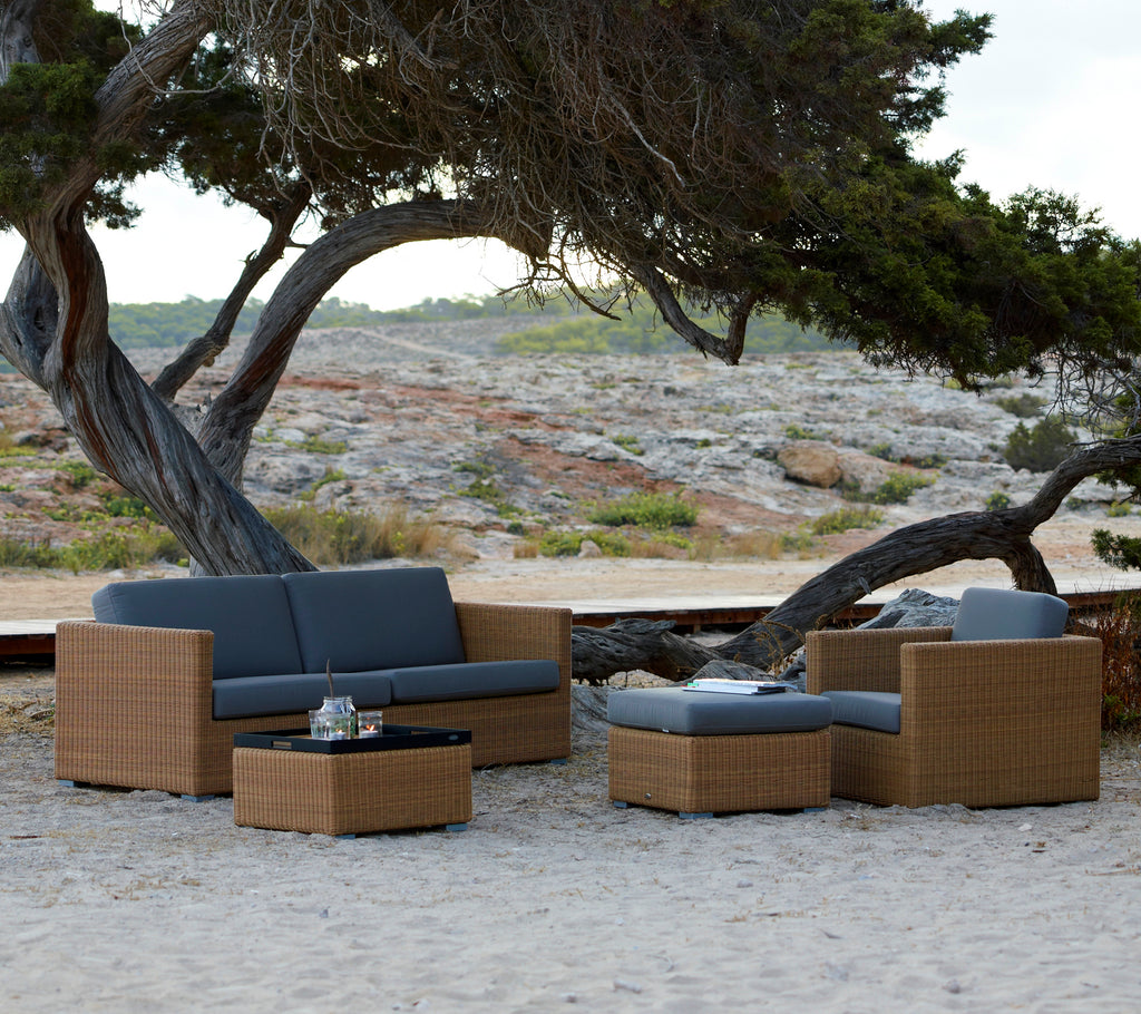 Mobilier de salon moderne marron avec des coussins gris, placé dans un environnement naturel en plein air.
