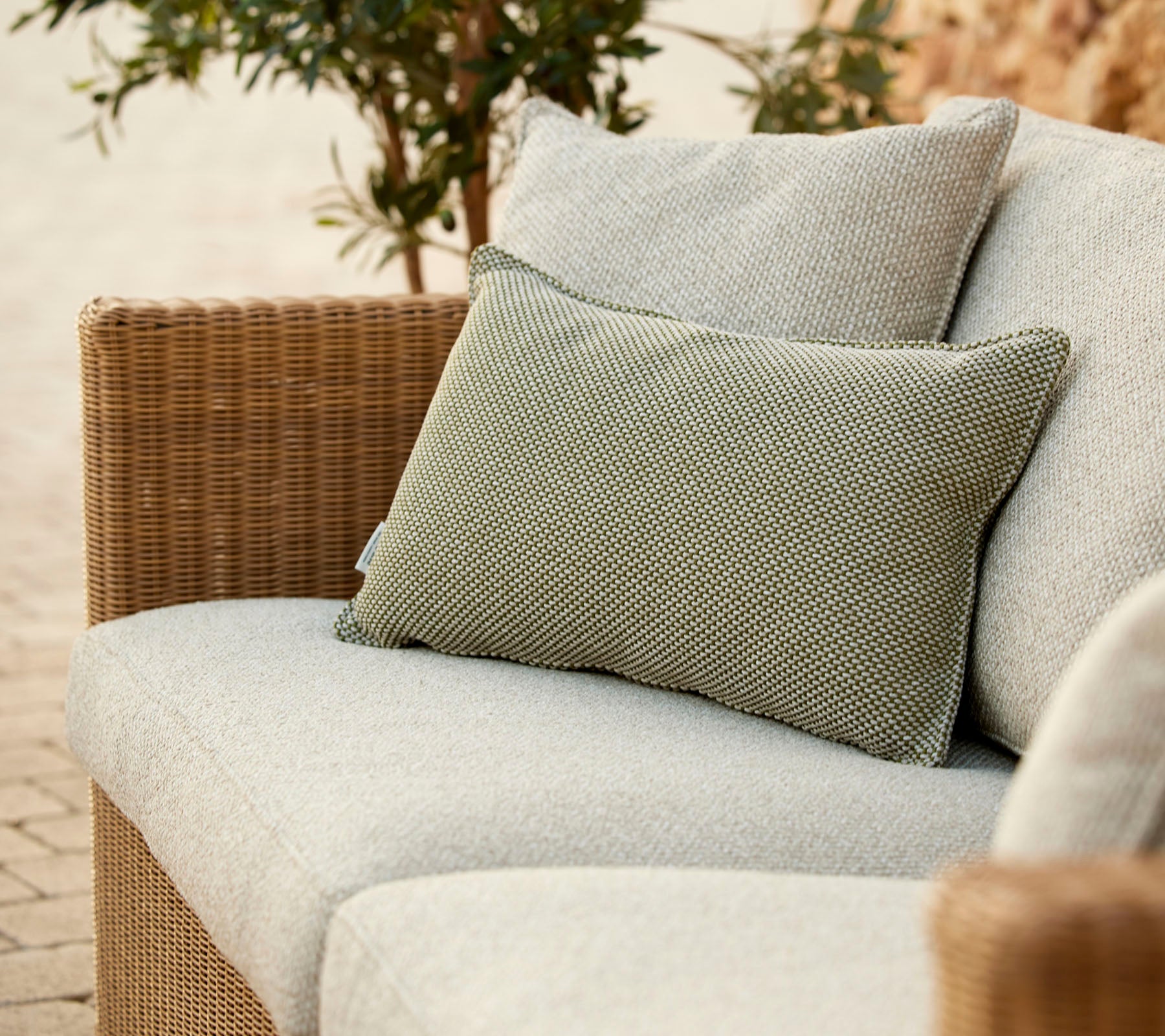 Un canapé élégant avec un coussin gris clair et un coussin vert texturé, entouré de verdure. Parfait pour se détendre.