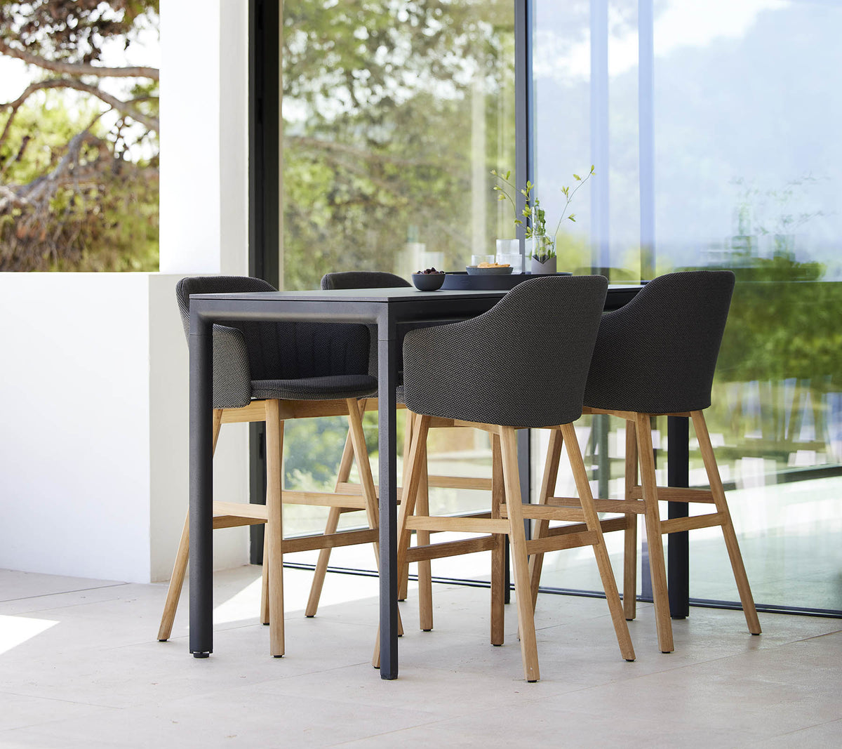 Une table de bar élégante accompagnée de quatre chaises de bar modernes avec des pieds en bois et des sièges rembourrés.