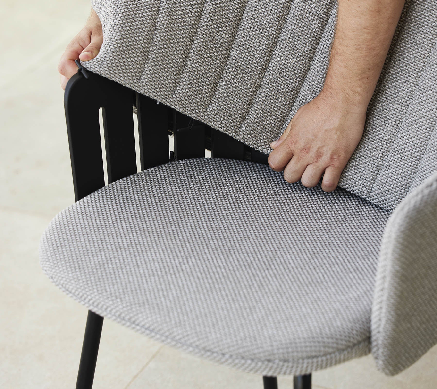Une personne ajuste le dossier d'une chaise moderne avec un siège en tissu texturé, mettant en avant un design élégant et un soutien ergonomique.