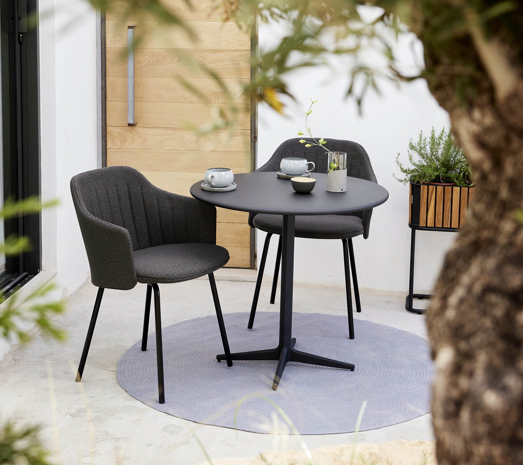 Chaise élégante et ensemble de table de café ronde, accompagnés d'une tasse et d'une soucoupe, entourés de verdure.