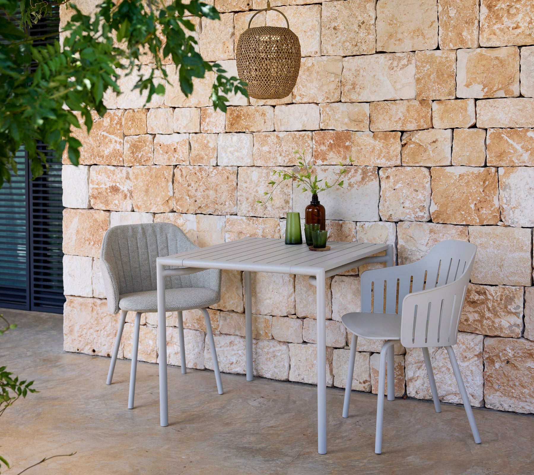 Table et chaises grises modernes avec des bouteilles vertes et brunes dans un cadre extérieur.