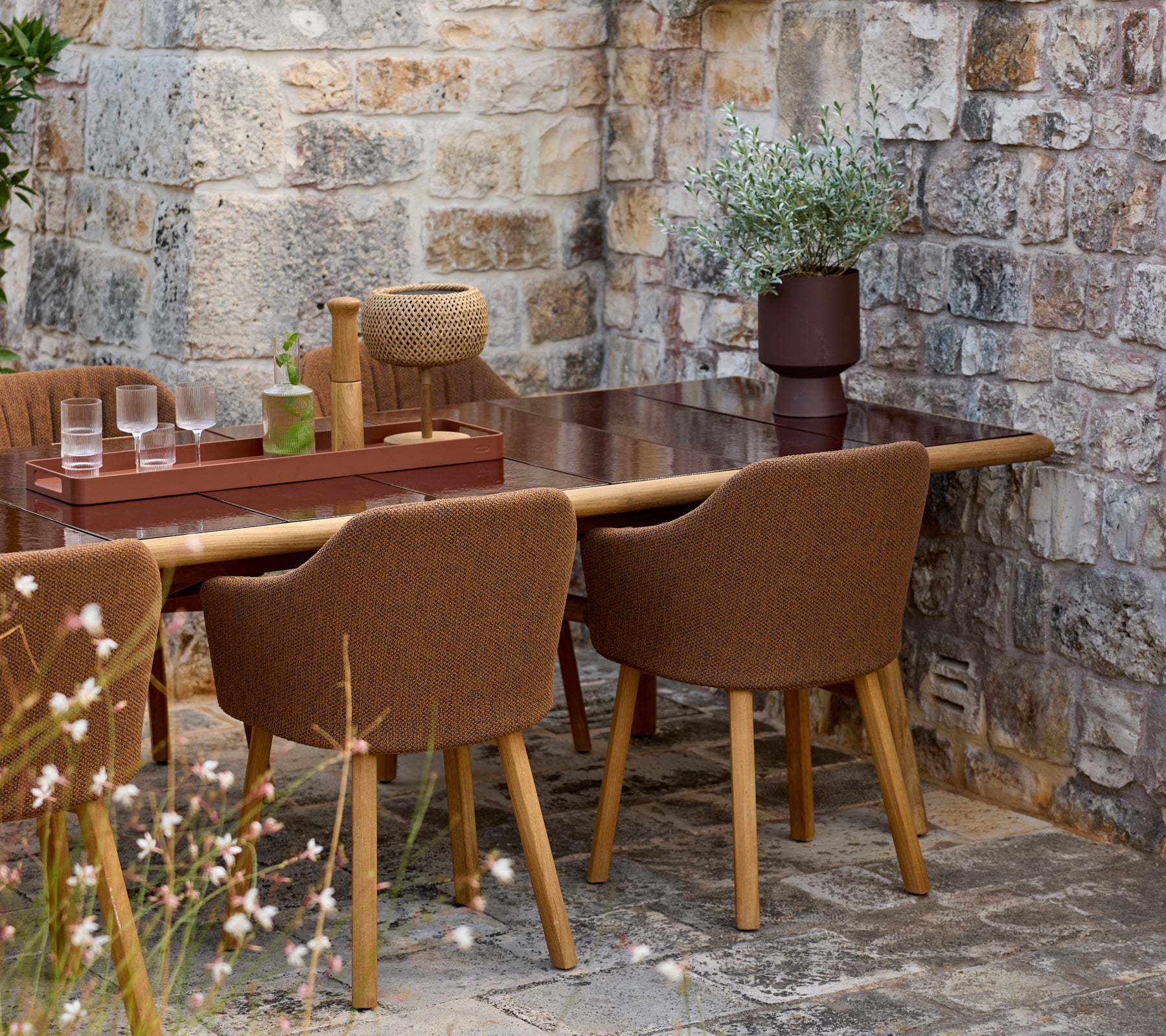 Des chaises brunes autour d'une table brune avec un vase décoratif dans un cadre extérieur.