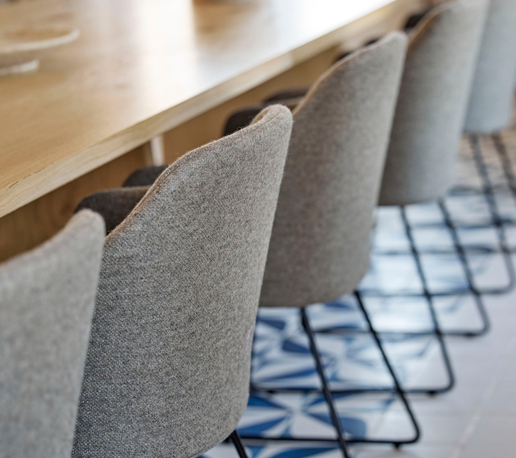 Une rangée de chaises élégantes et rembourrées avec des pieds en métal fins, positionnées autour d'une table en bois, avec un sol à motifs en dessous.