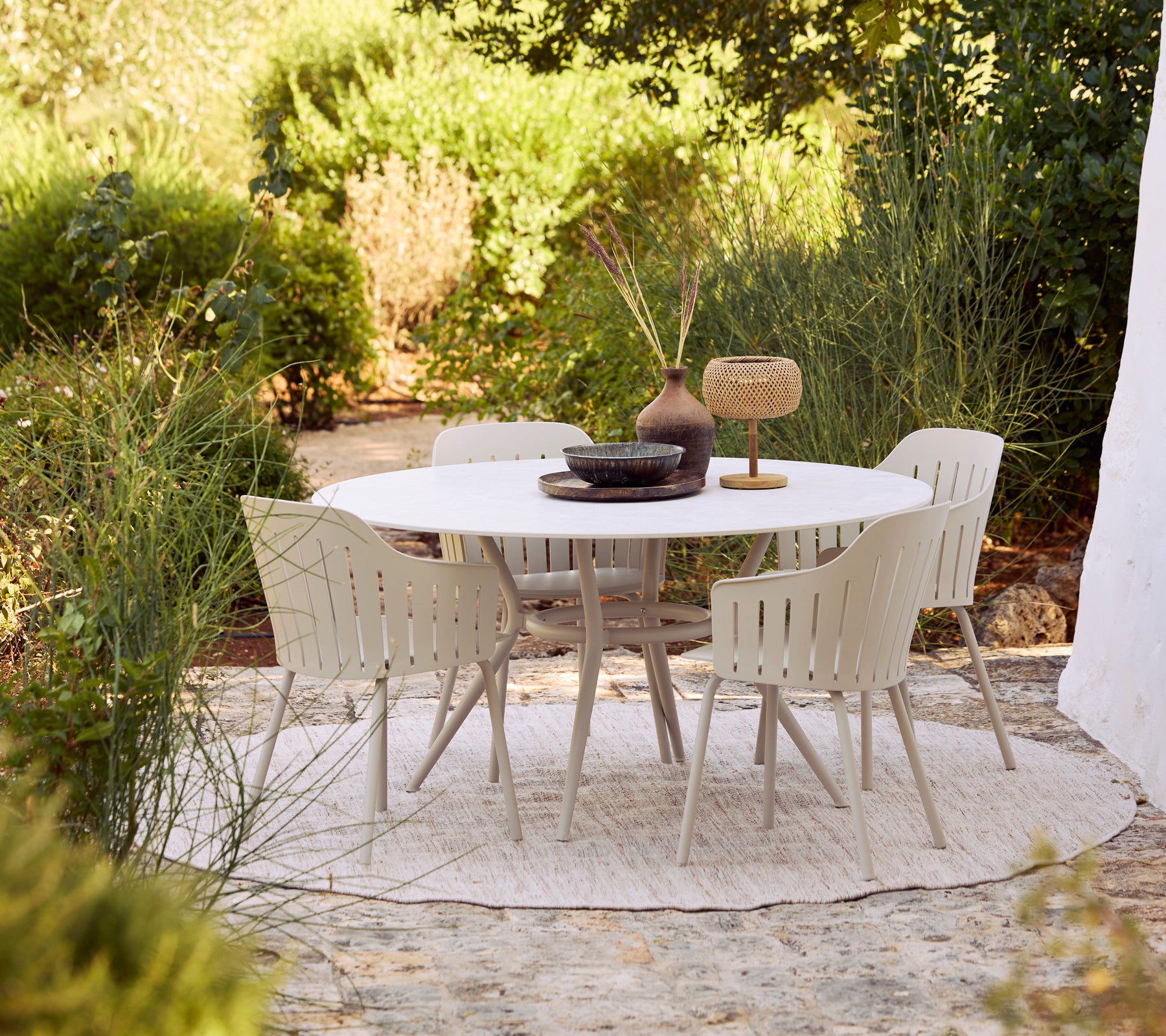 Ensemble de salle à manger d'extérieur avec une table ronde blanche et des chaises beiges entourées de verdure.