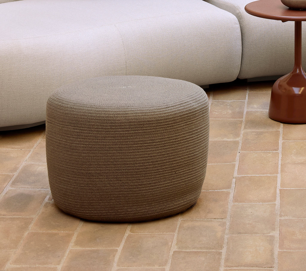 Petit pouf circulaire taupe avec une surface texturée, complétant les styles de meubles et de décoration contemporains.