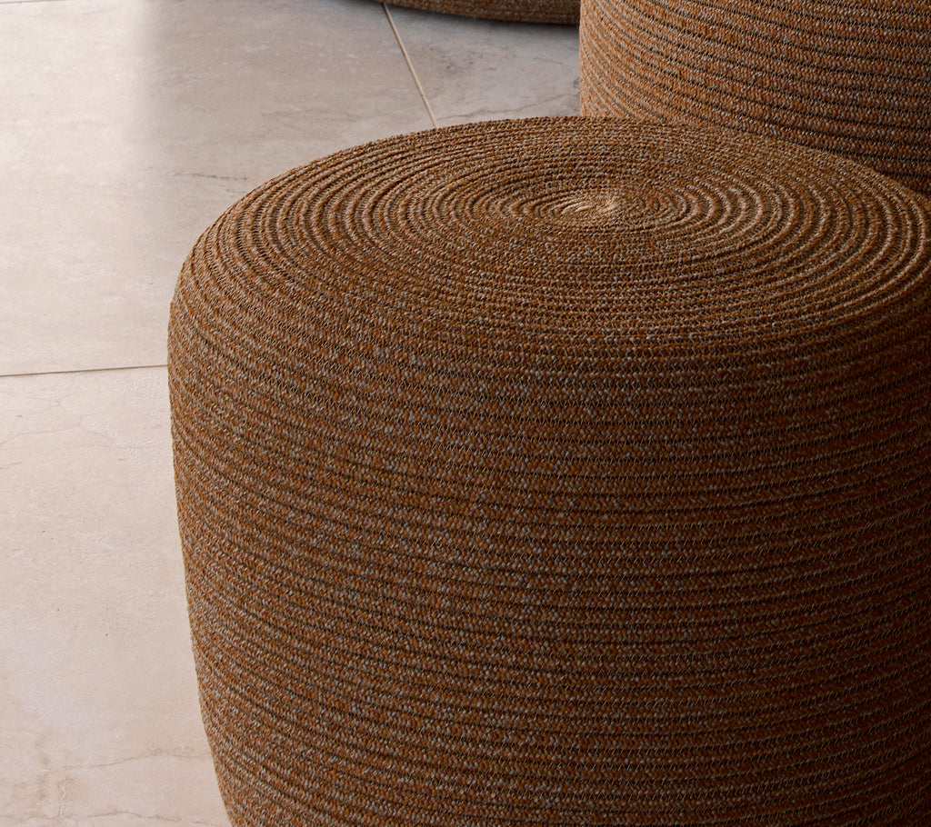 Petit pouf circulaire brun ombre avec une surface texturée tissée, offrant un accent élégant pour l'assise ou la décoration.