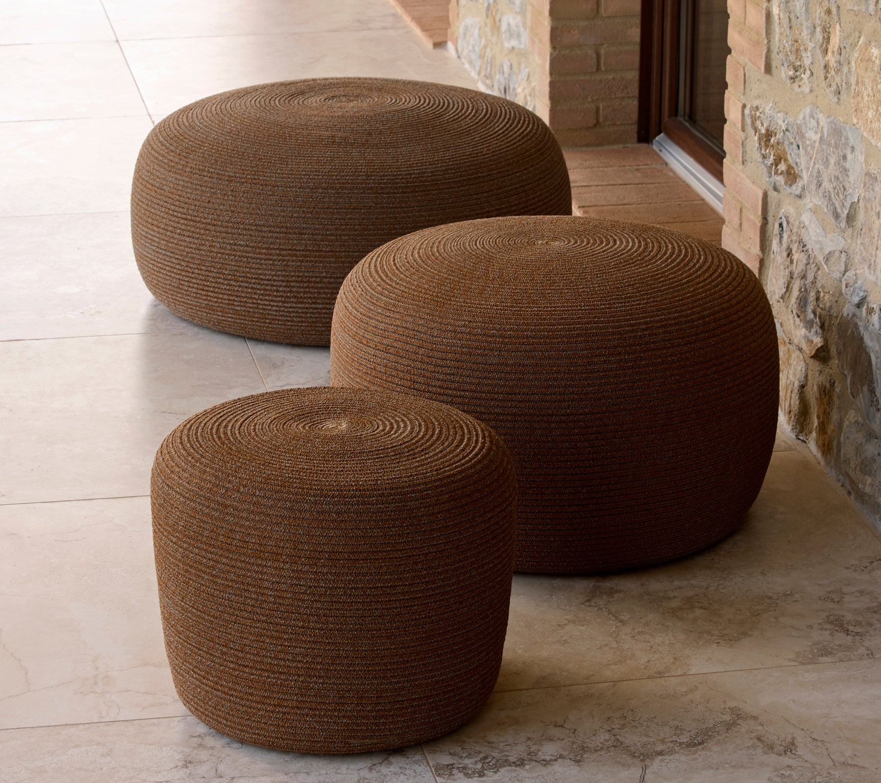 Trois poufs ronds en brun umbre, de tailles variées, avec une surface texturée et une forme ronde, arrangés ensemble.