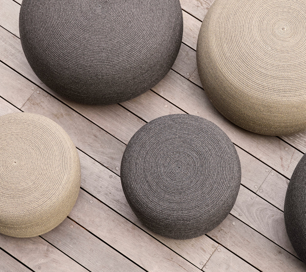 Une collection de poufs ronds de tailles variées et de couleurs neutres disposés sur une surface en bois.