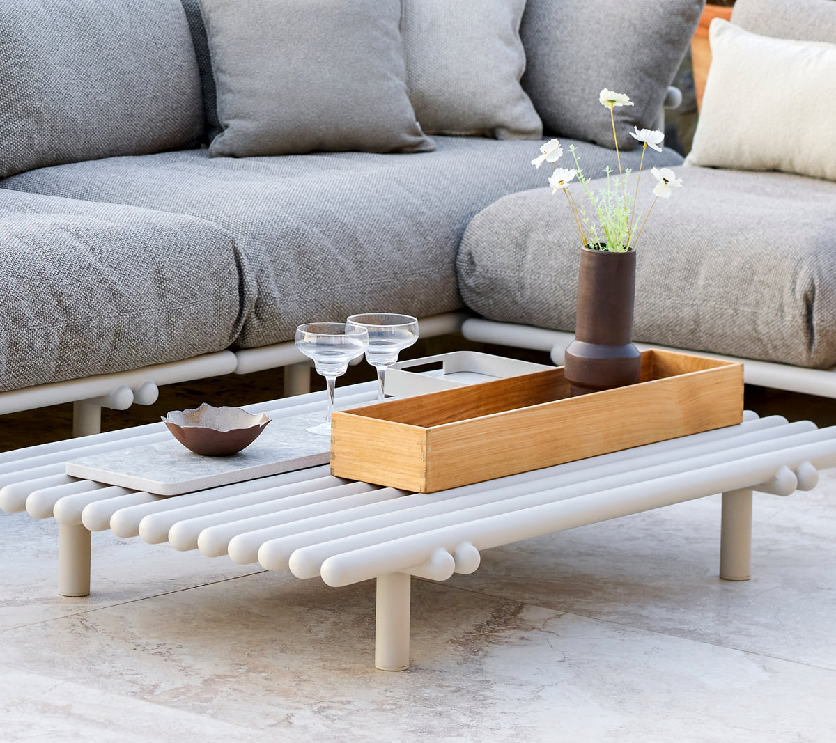 Une table basse élégante avec une boîte de rangement en teck, présentant un design minimaliste et des éléments décoratifs tels que des verres et un petit vase.