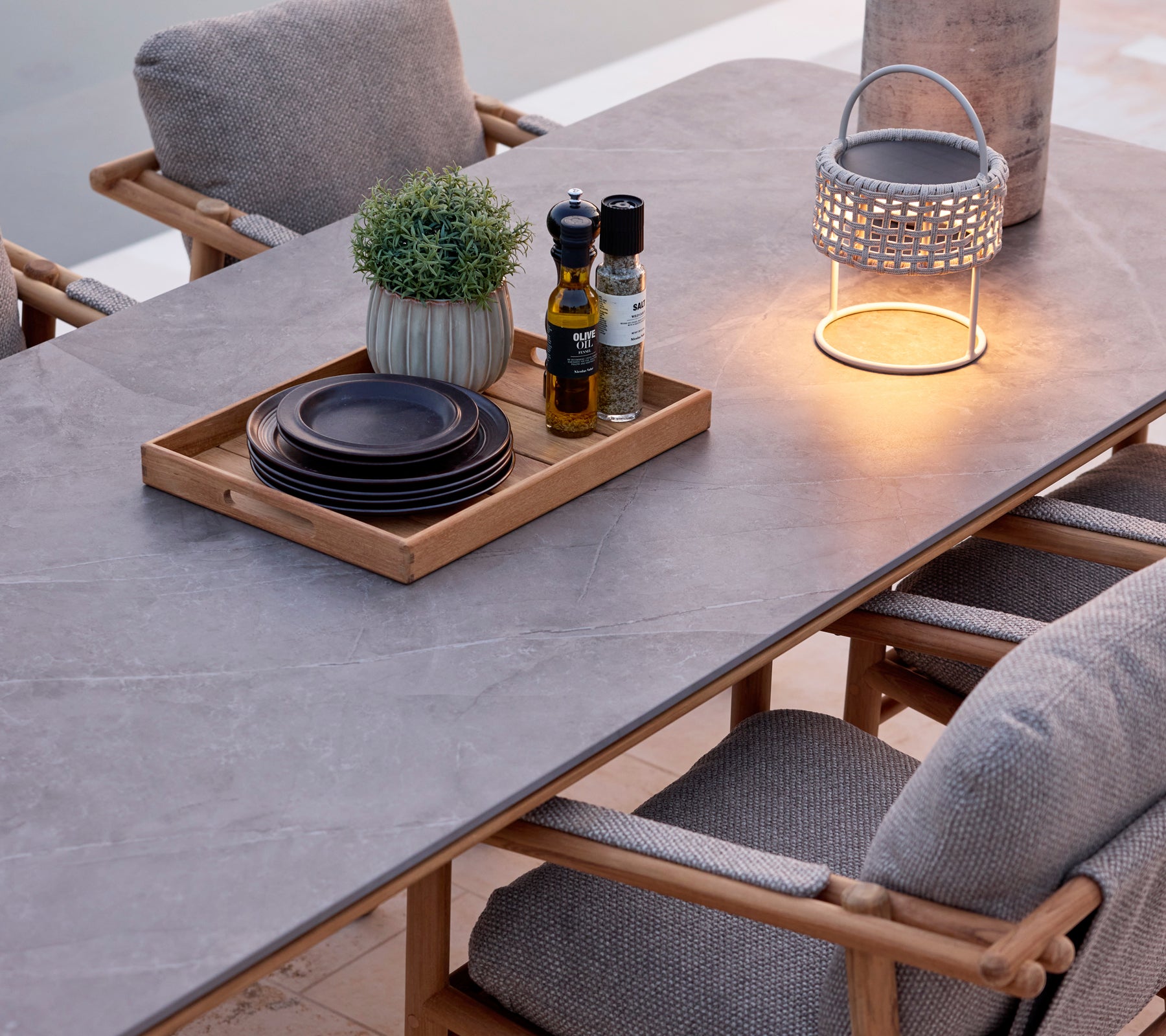 Table à manger moderne avec surface grise, chaises brunes, assiettes noires et une lanterne décorative.