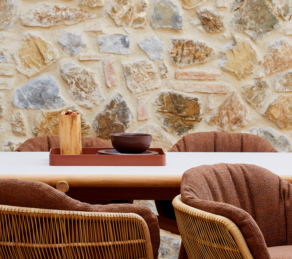 Un aménagement cosy avec un plateau de club rouge désert, un bol marron et des chaises tressées élégantes devant un mur en pierre.