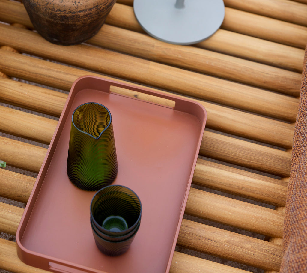 Un petit plateau rectangulaire rouge avec deux verres verts, reposant sur une surface en bois avec des éléments décoratifs supplémentaires à proximité.