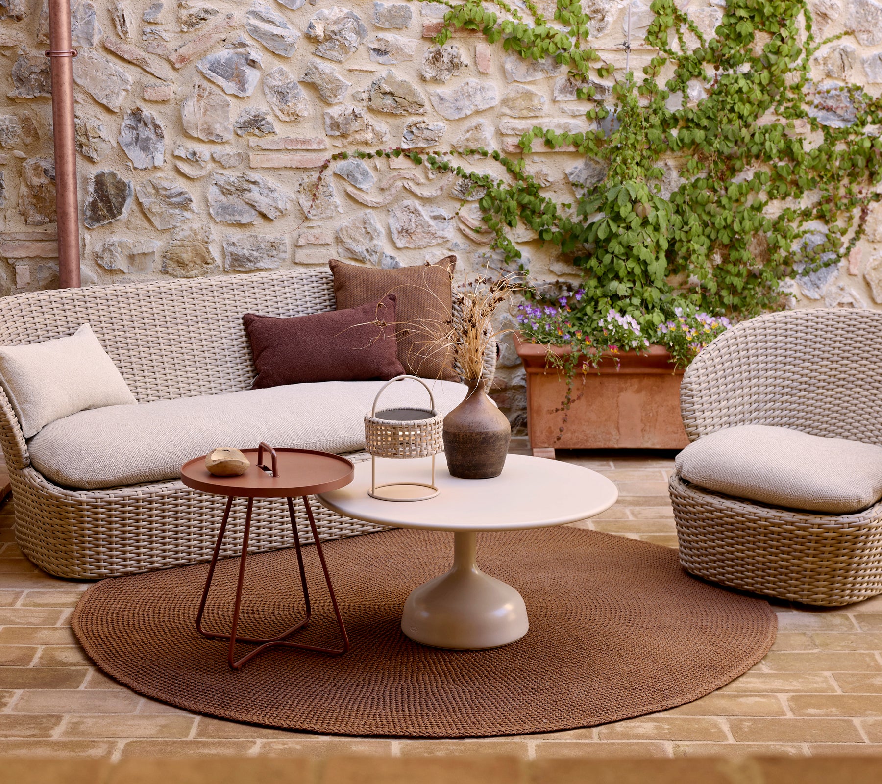Espace salon confortable avec un tapis tricoté, une table basse brillante et une table d'appoint élégante, rehaussé de coussins décoratifs et de verdure.