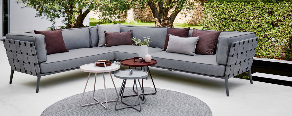 Canapé sectionnel conique moderne en tissu gris avec des coussins décoratifs, accompagné de tables d'appoint élégantes et d'un tapis rond.